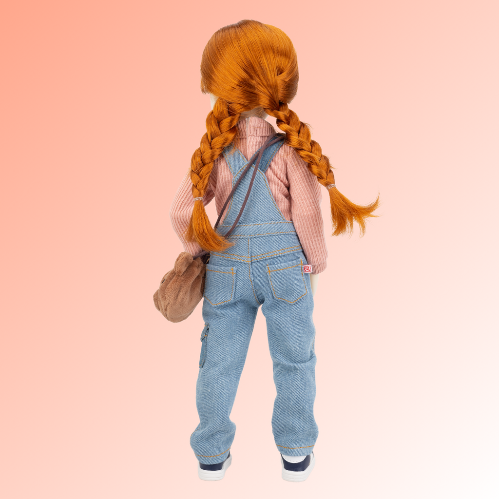 New ruby red core line doll Tina, wearing salmon coloured button up shirt and overalls with blue lace up sneakers and a teddy bear bag.
